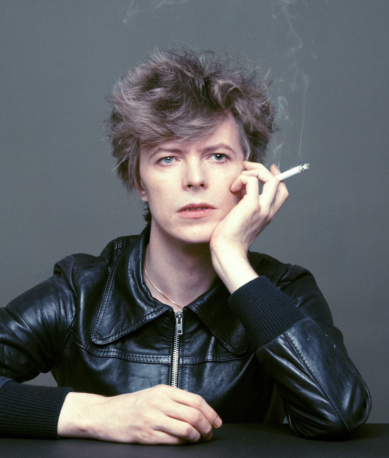 Artisten David Bowie klädd i svart skinnjacka röker en cigarett. 