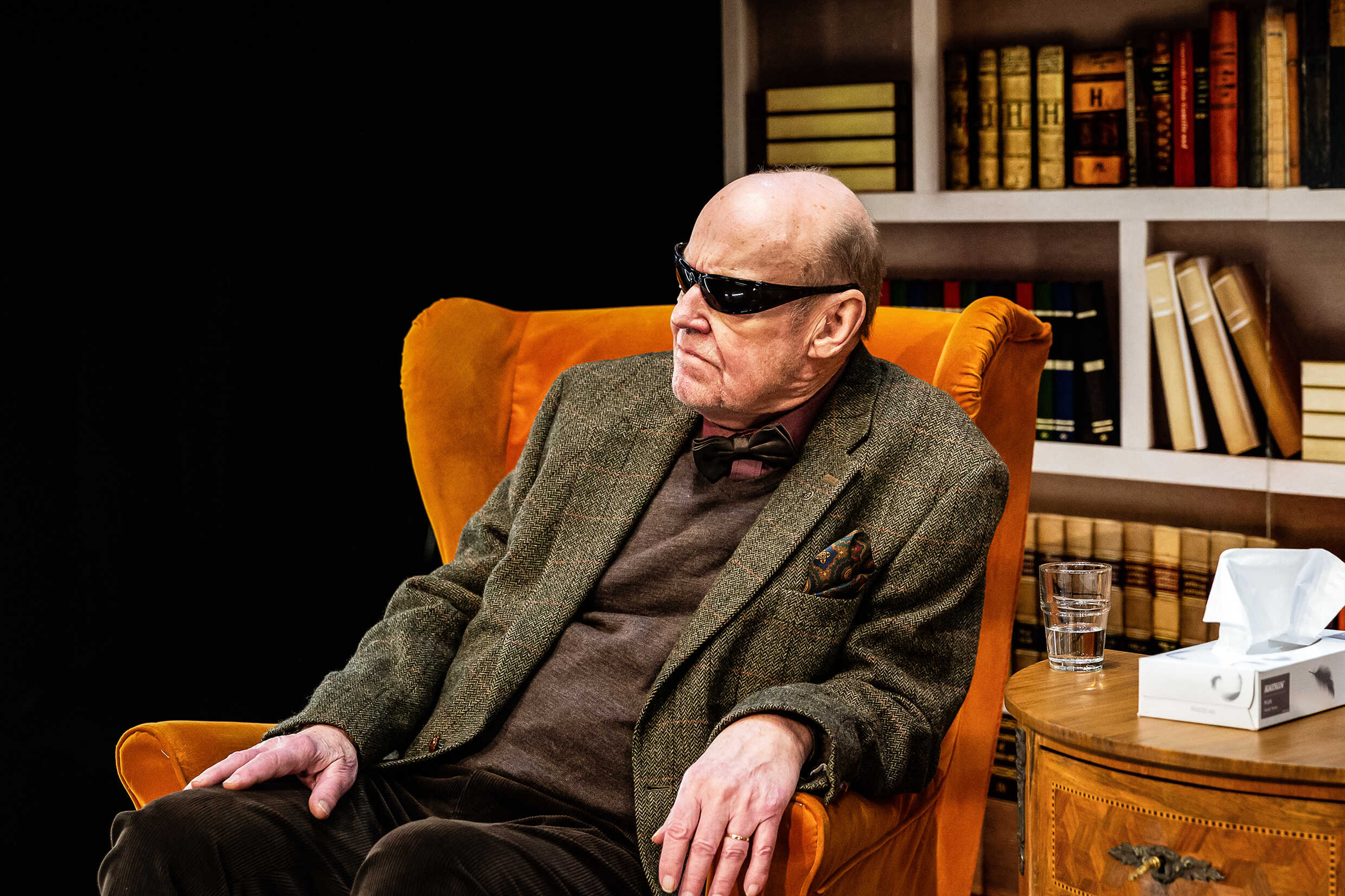 En äldre man i en fåtölj i ett terapirum spelad av Sten Ljunggren. Han har svarta solglasögon på sig 