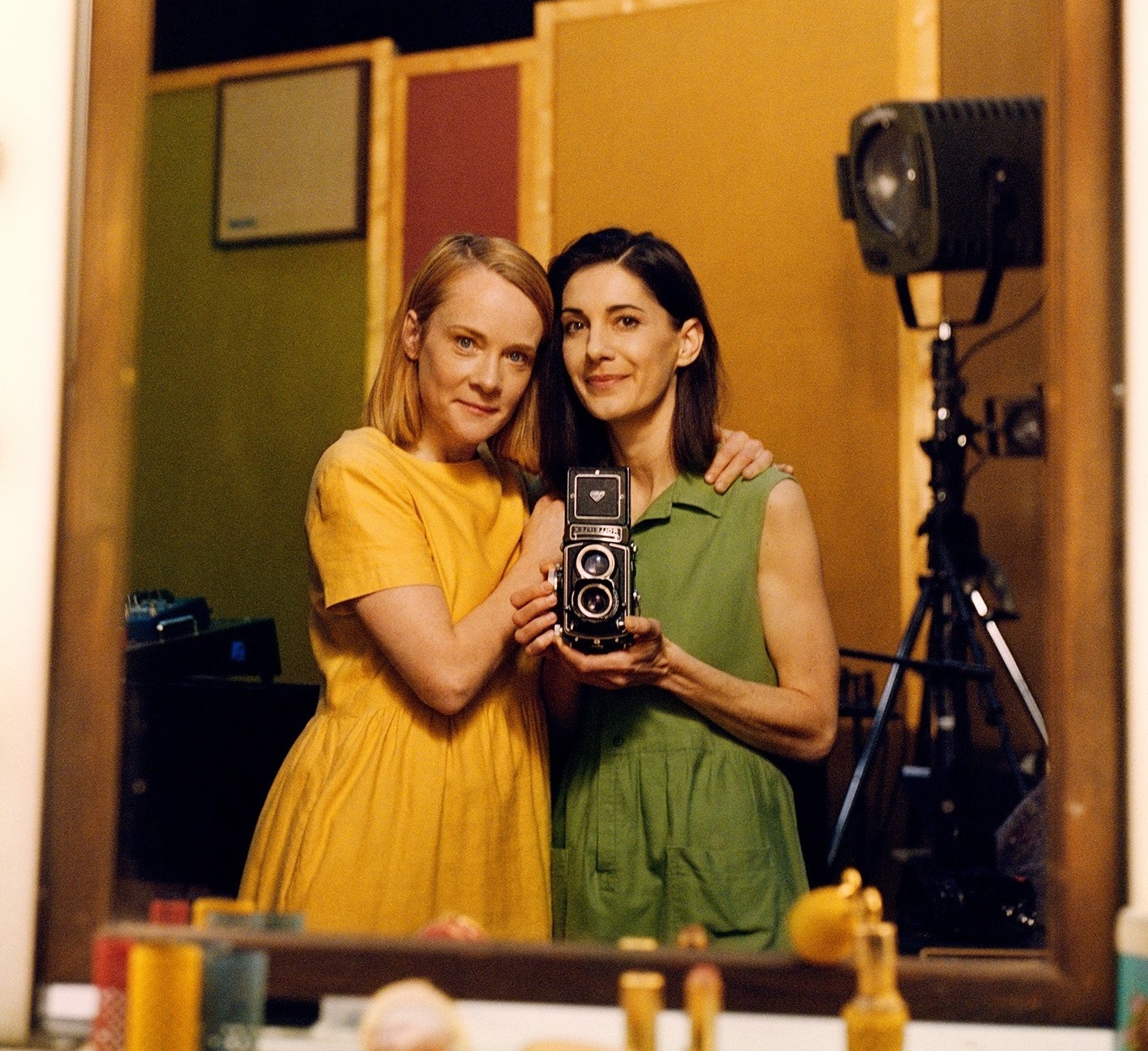 Två kvinnor fotograferar sig själva i en spegel med en kamera av äldre modell. 
