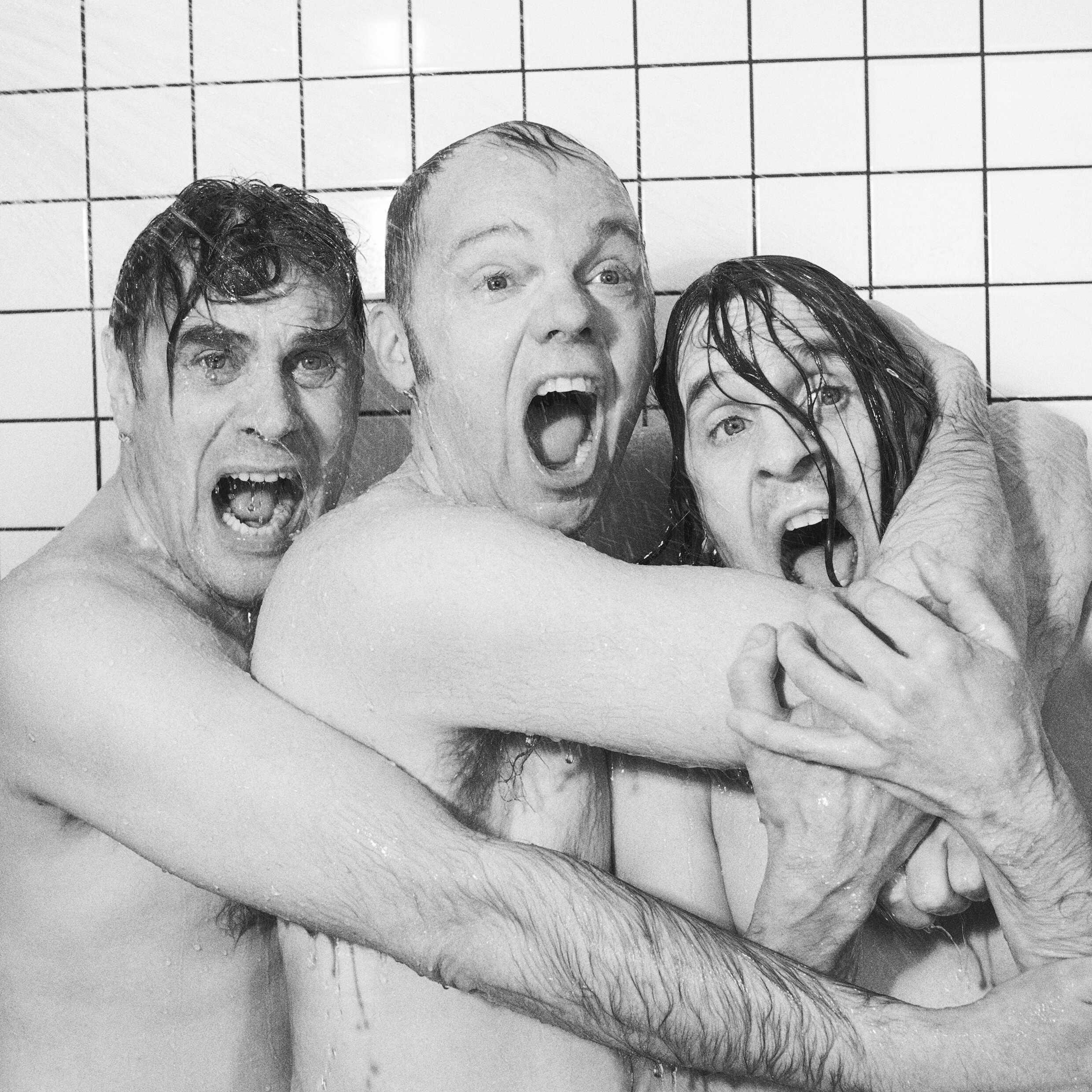 Tre män håller om varandra i en dusch och skriker. 