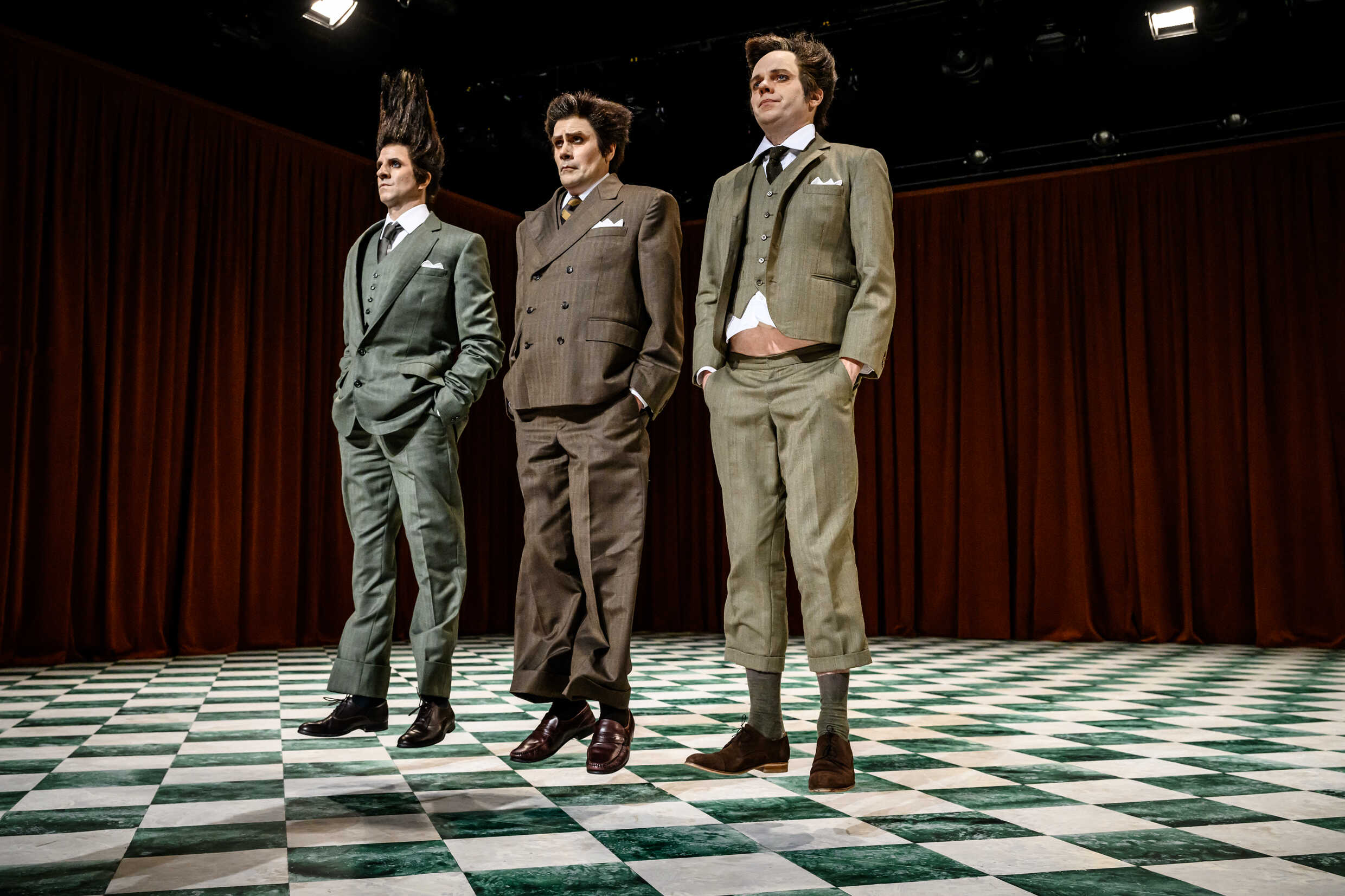 Tre skådespelare klädda i kostym hoppar på en scen. 