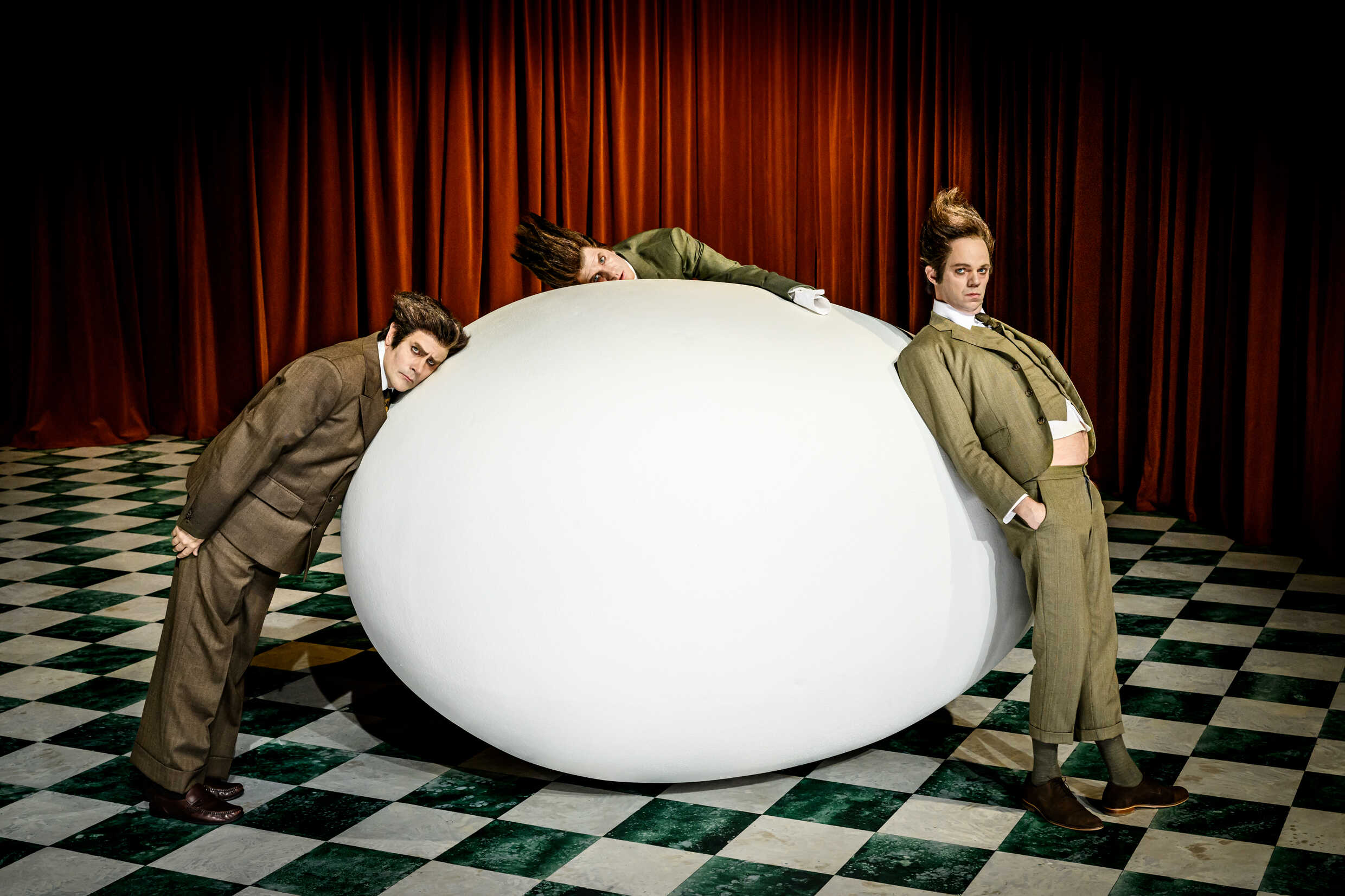Tre skådespelare och en stor vit oval form på en scen. 