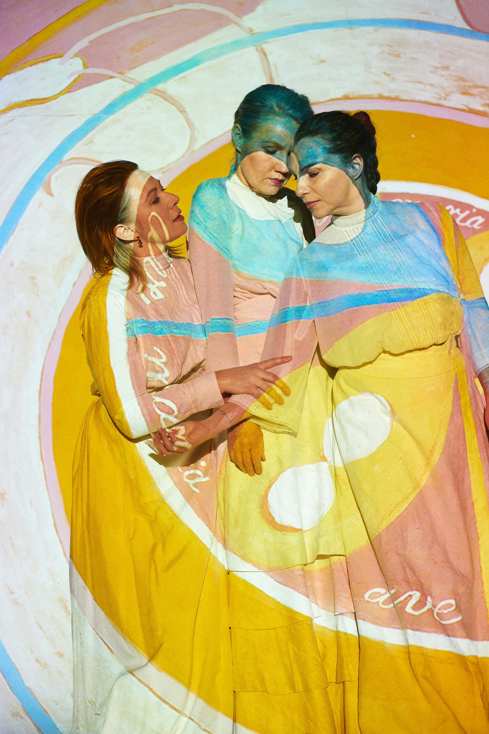 Tre kvinnor ser ut att vara inuti en målning i olika abstrakta mönster. 