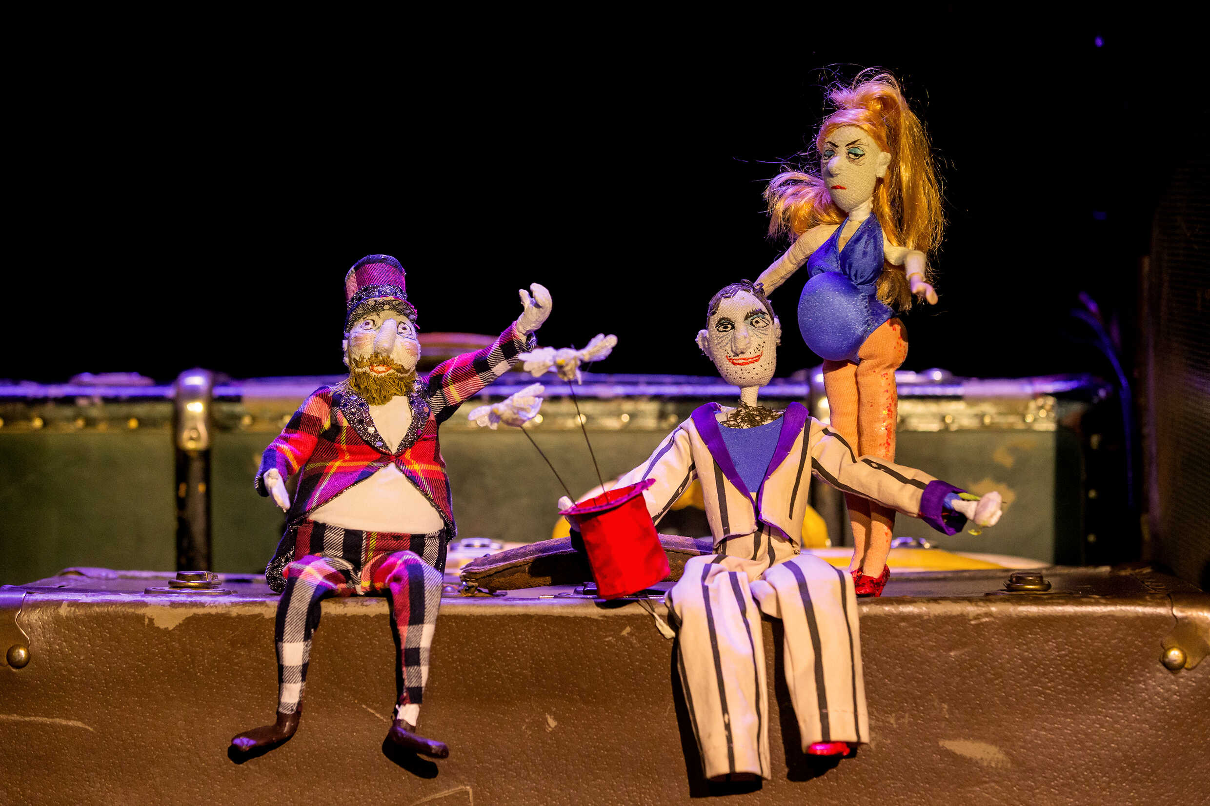 Tre dockor som medverkar i föreställningen sittandes på resväskor